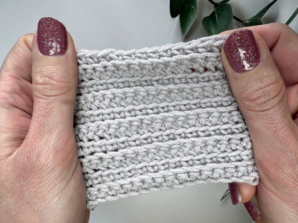two hands hold a grey crochet fabric showing alternating front and back loop single crochet stitches