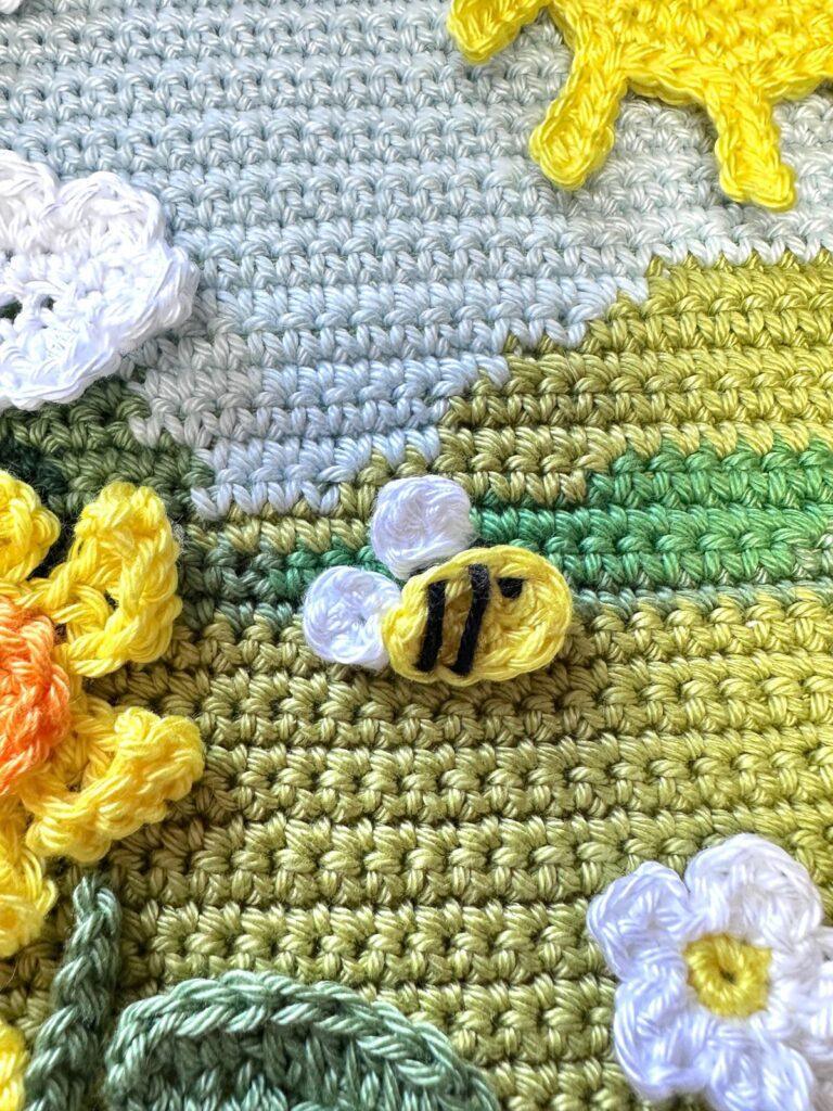 a crochet bee is sewn onto a crochet garden landscape