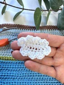 A hand holds a small white crochet cloud above a crochet blue background