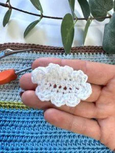 A hand holds a small white crochet cloud above a crochet blue background