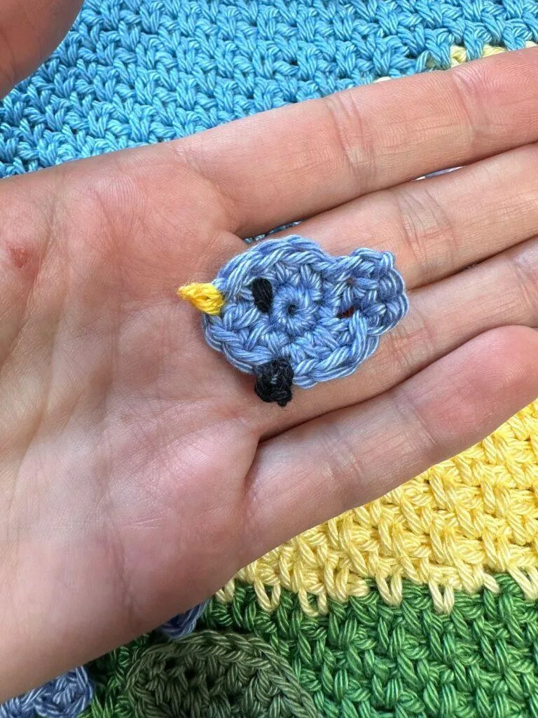 a tiny crochet chick in blue is laid on a flat hand