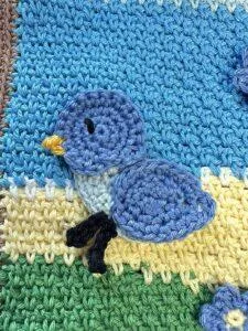 a crochet bird appliqué is sewn on a blue and yellow background