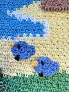 2 tiny crochet blue chicks are placed on a crochet seaside landscape