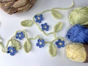 a crochet flower and leaf garland is laid out on a white surface with yarn to the side