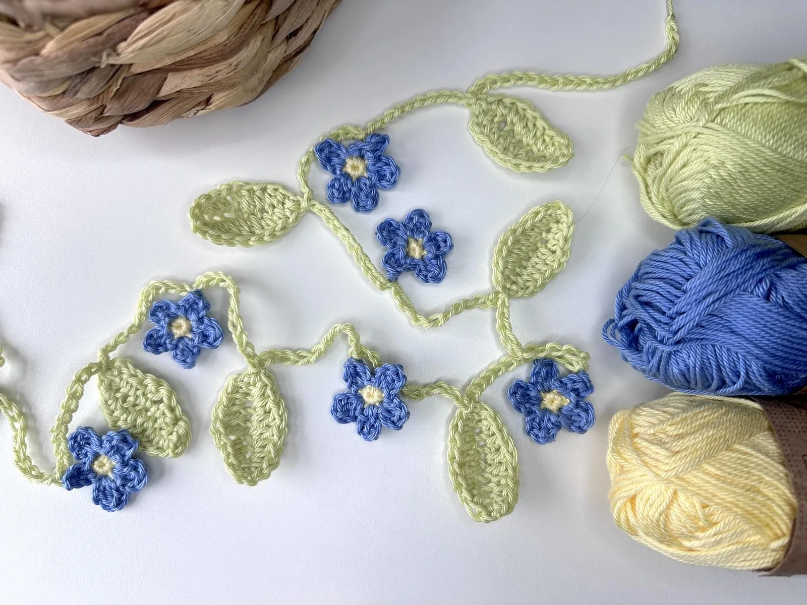 a crochet flower and leaf garland is laid out on a white surface with yarn to the side