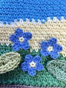 3 crochet forget me nots are on a crochet scene background