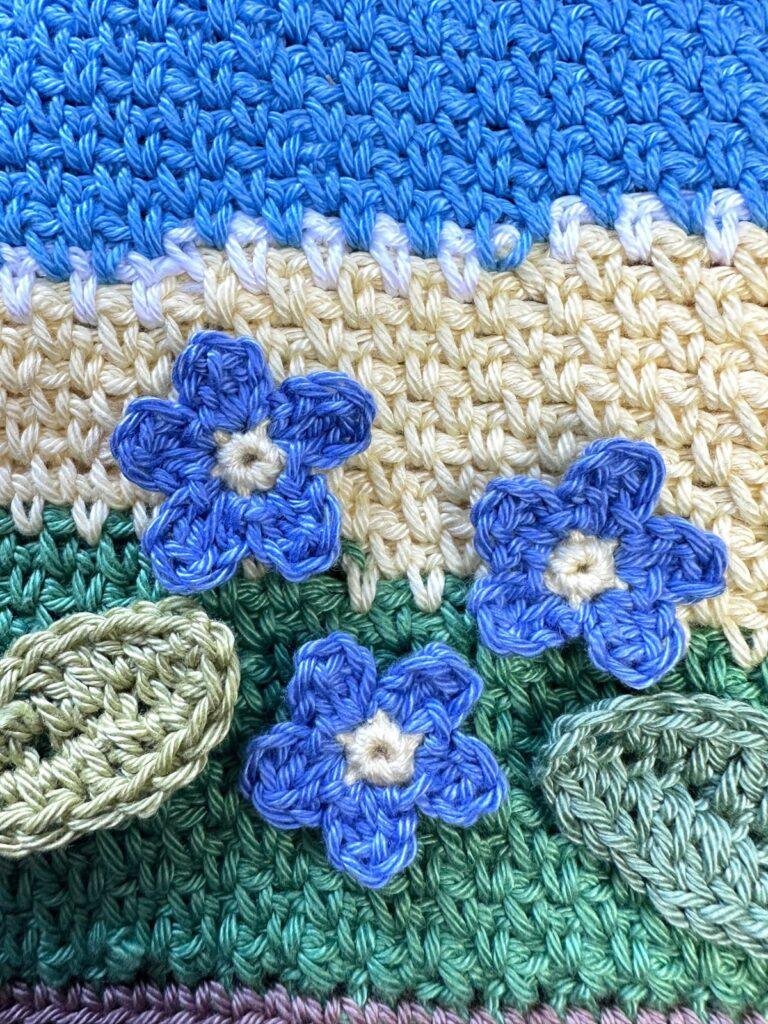 3 crochet forget me nots are on a crochet scene background