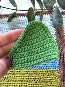 A hand holds a green crochet hill applique patch