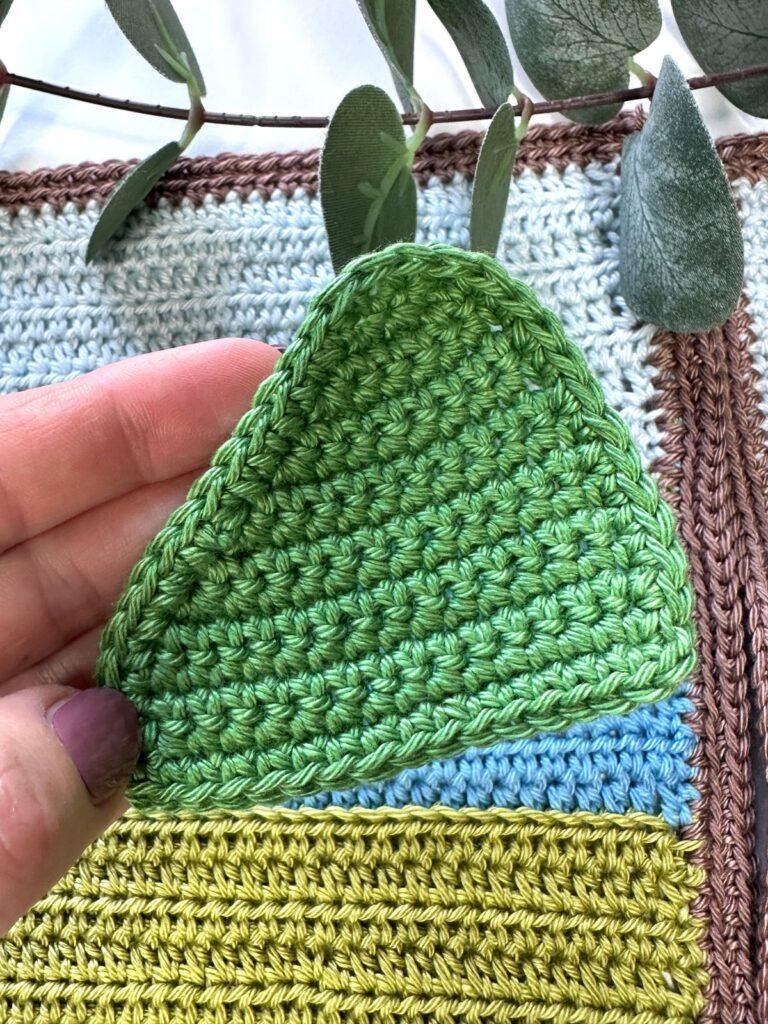 A hand holds a green crochet hill applique patch