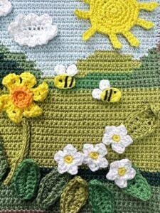 A spring crochet scene featuring crochet pansies, bees and sun