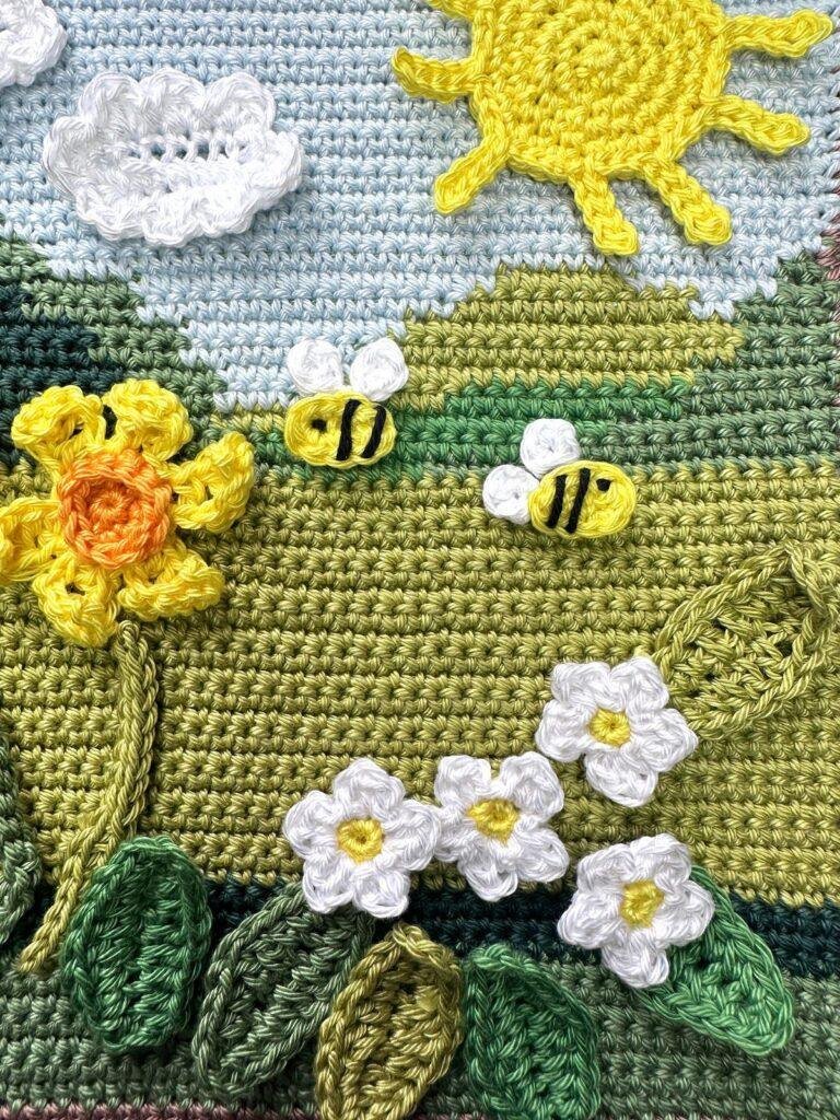A spring crochet scene featuring crochet pansies, bees and sun