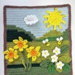 a crochet hill scene with spring flowers, bees and sun