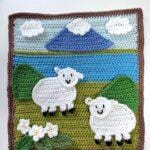 A spring crochet scene of a lake, mountain, hills and sheep