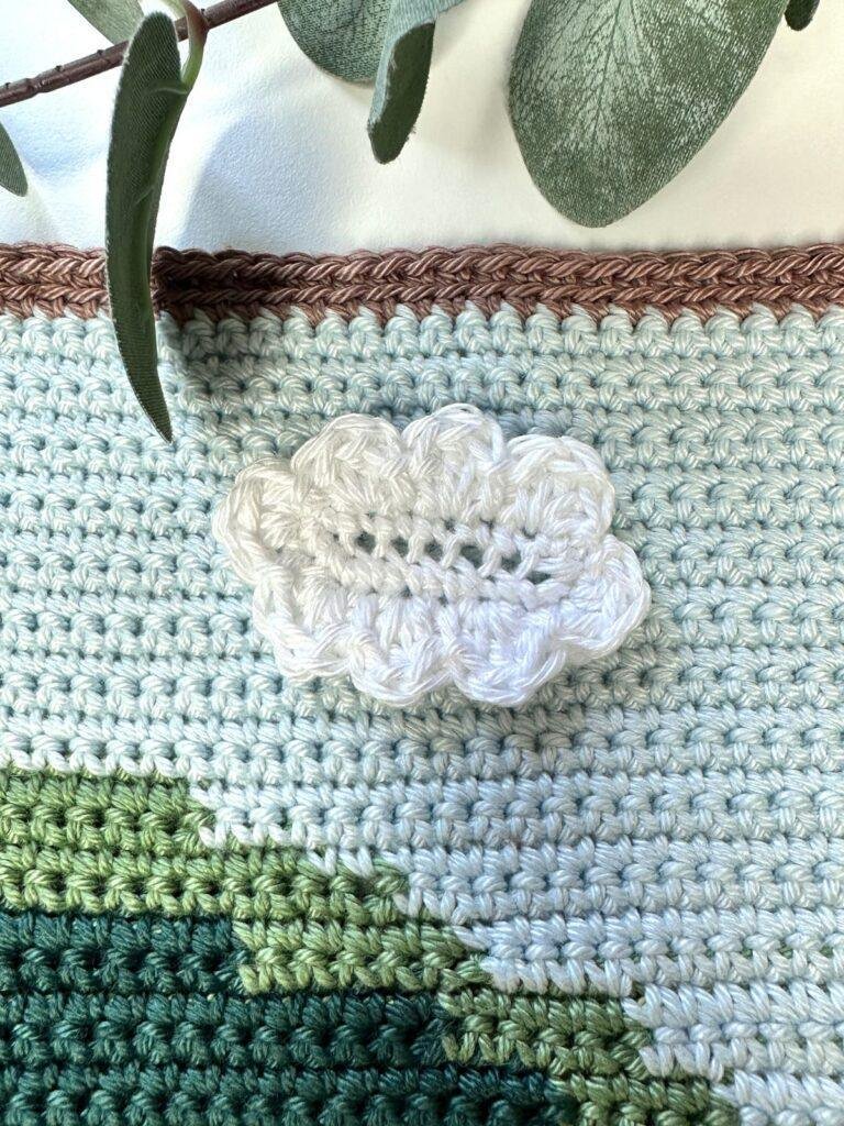 A crochet cloud applique is sewn onto a crochet background of blue and green