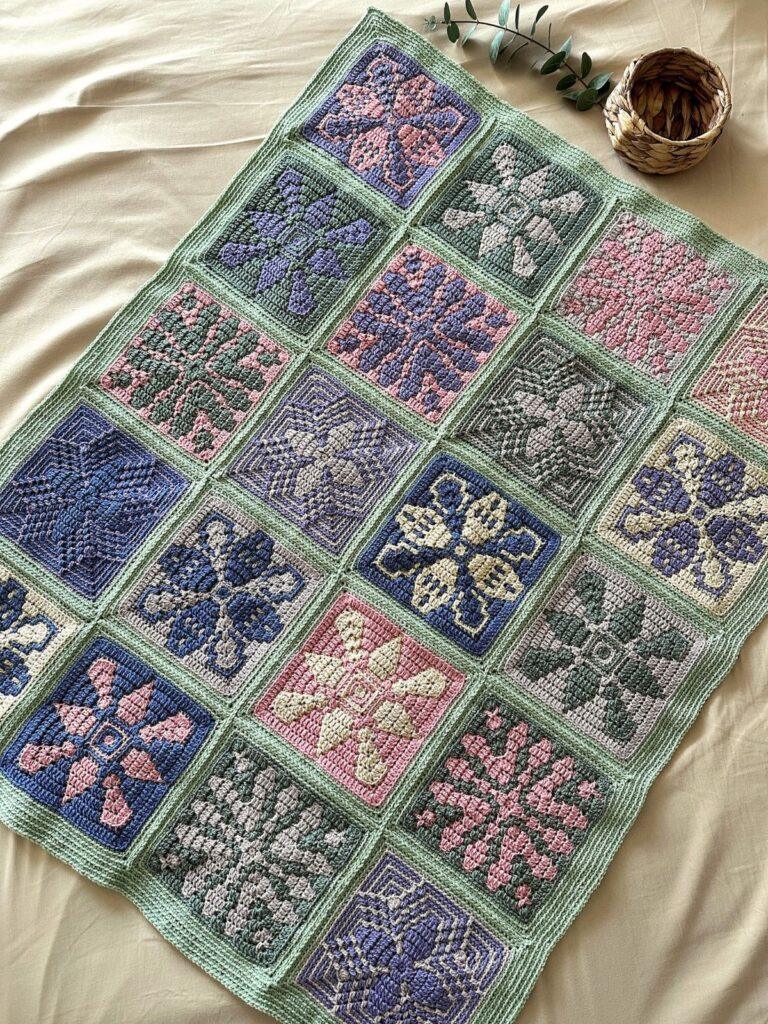 A mosaic crochet blanket made of different crochet tiles with flowers on is laid out on a cream surface