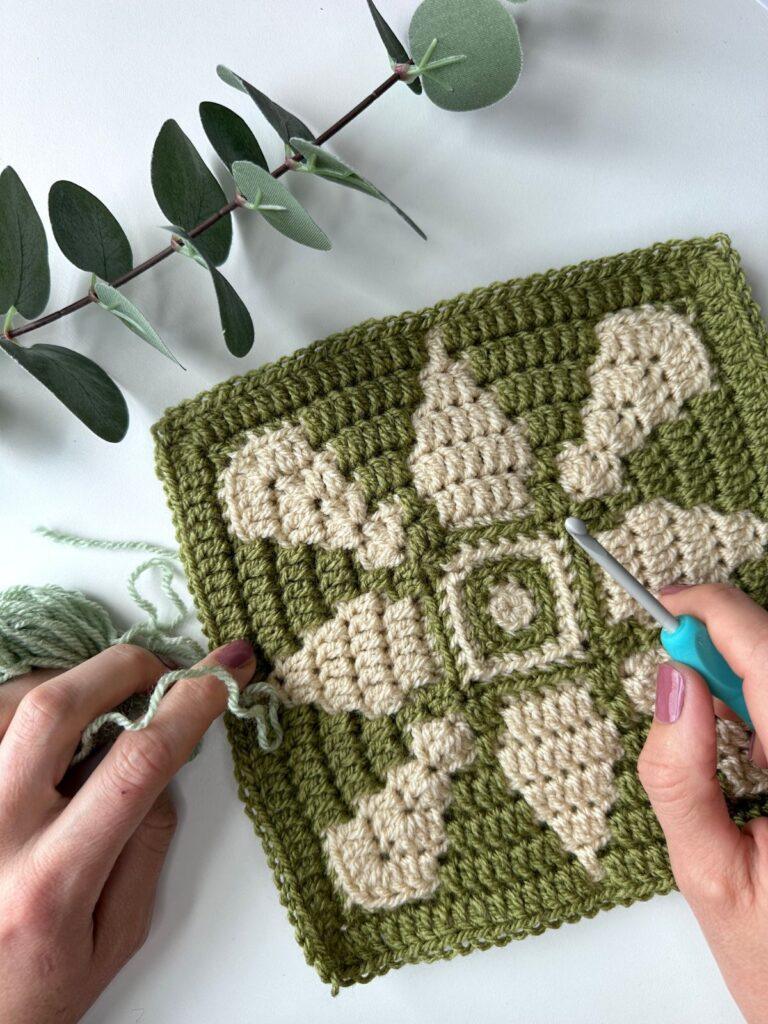 A green and cream mosaic crochet square with a flower motif