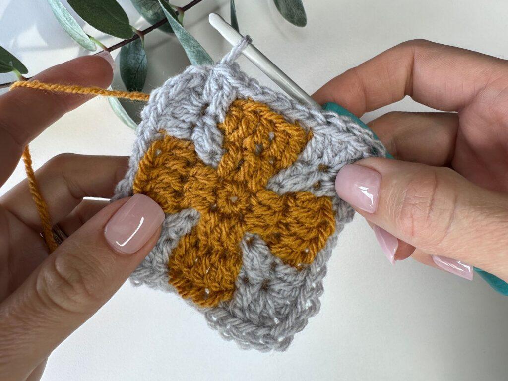 2 hands are crocheting a mosaic crochet square from the center out, focussing on the corner