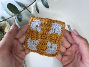 2 hands hold a yellow and grey crocheted tile made using mosaic crochet in the round