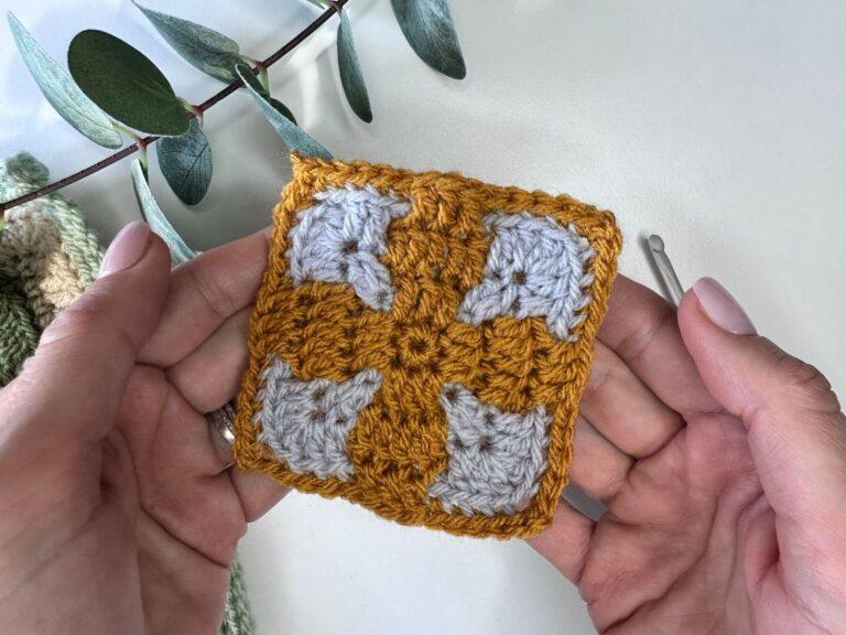 2 hands hold a yellow and grey crocheted tile made using mosaic crochet in the round