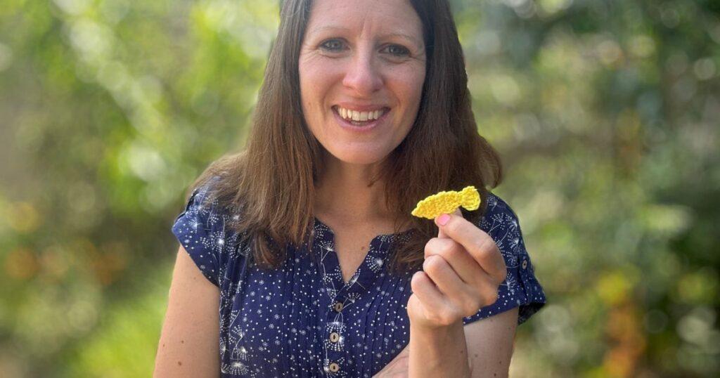 A lady holds a tiny crochet fish applique made of yellow yarn