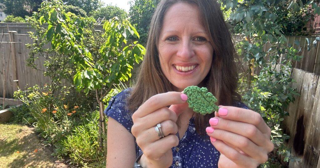 A lady holds a green crochet daisy leaf in her hands
