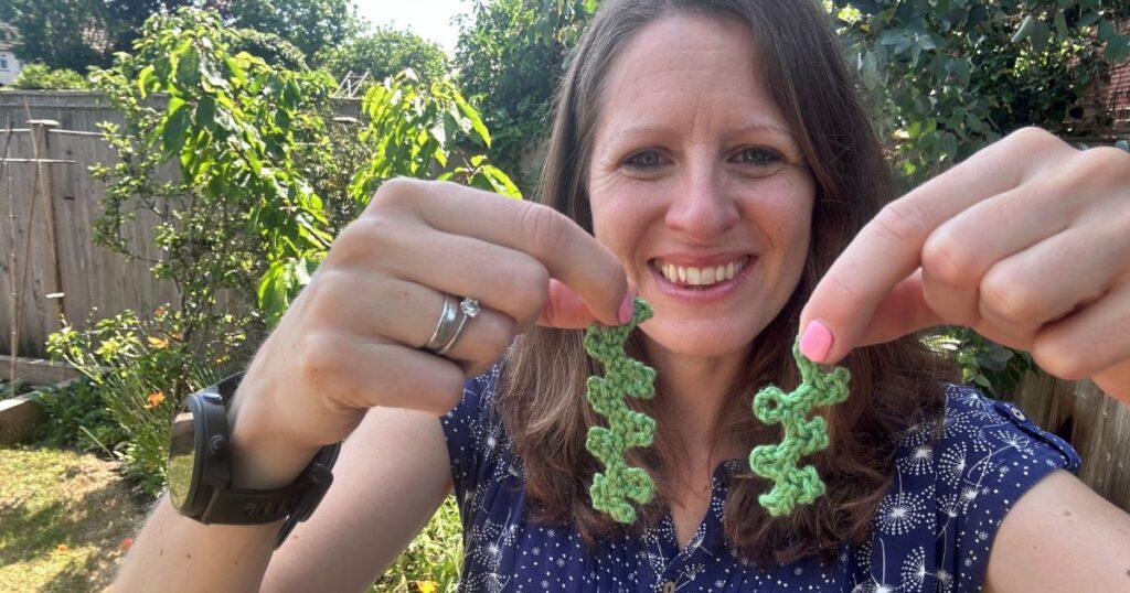 A woman holds up 2 strands of crochet seaweed