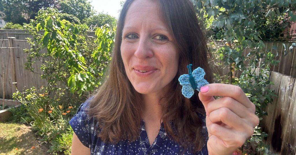 A lady holds a small blue crochet butterfly