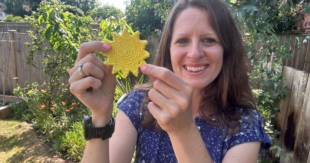 A lady smiles and holds a yellow crochet sun