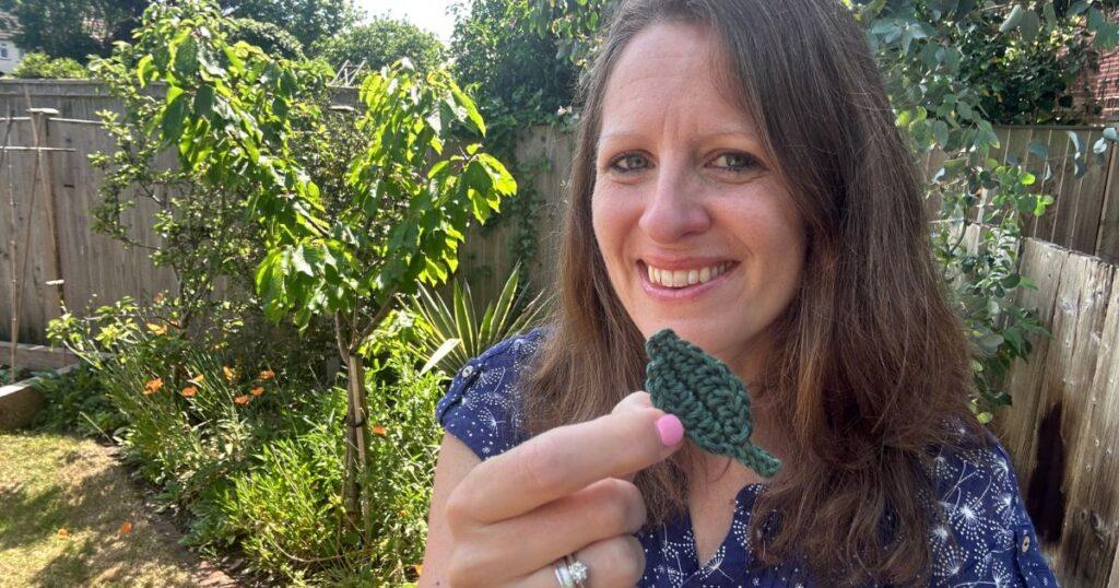 A lady holds a small green crochet leaf in front of her