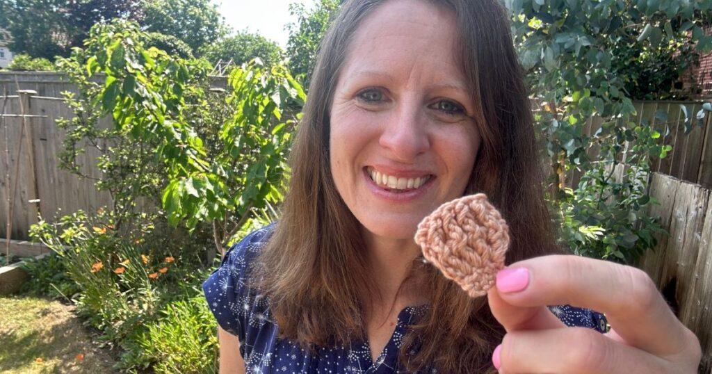 A person holds up a small crochet shell in beige yarn with textured stitches.