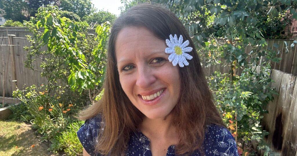 A person has a yellow and white crochet daisy in her hair