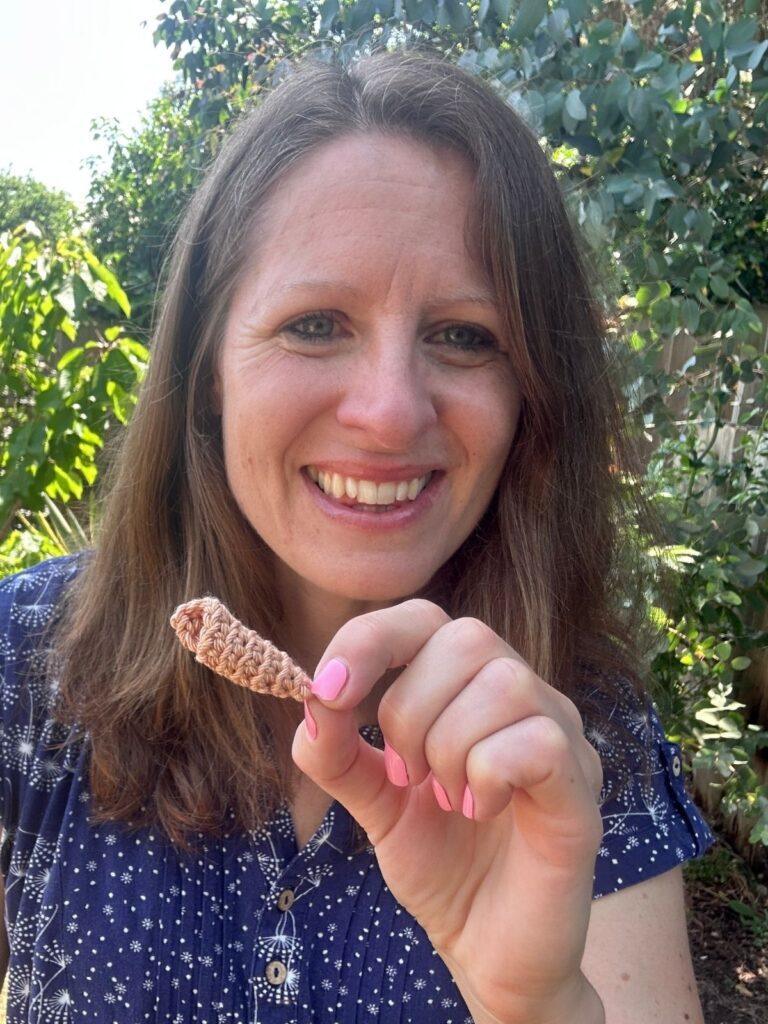 A woman holds a tiny crochet conch shell in her hand