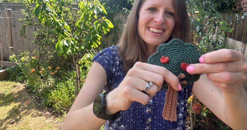 A lady holds a crochet applique tree with small red crochet apples on it