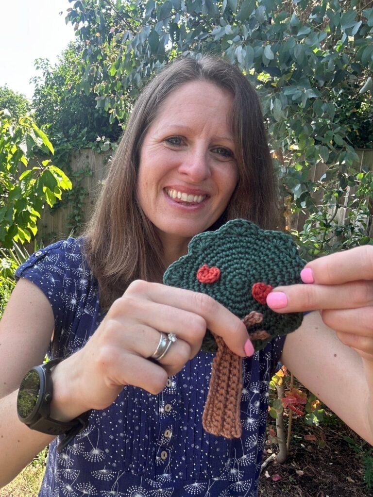 A lady holds a crochet applique tree with apples on