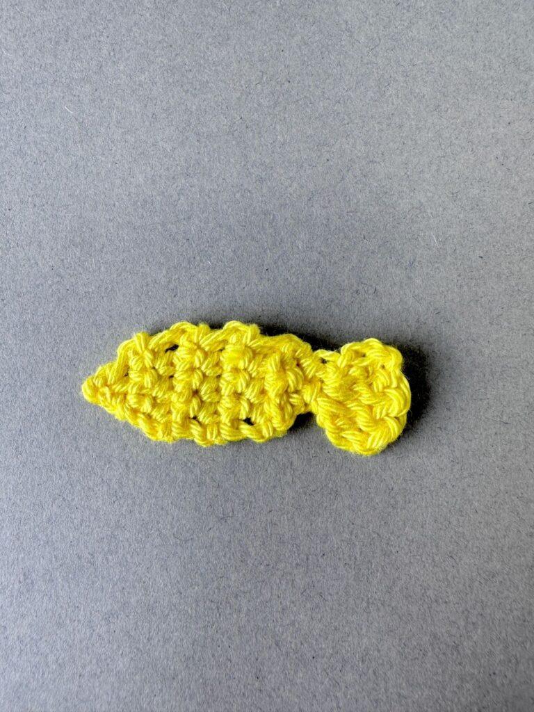 A simple yellow crochet applique fish on a grey background