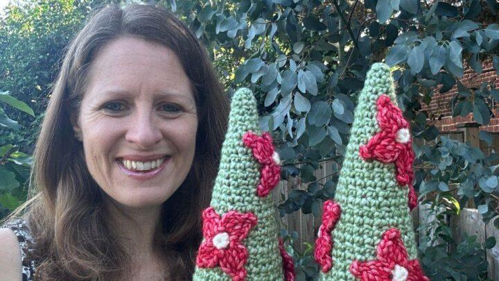 A lady holds 2 crochet Christmas tree cones with red flowers on them