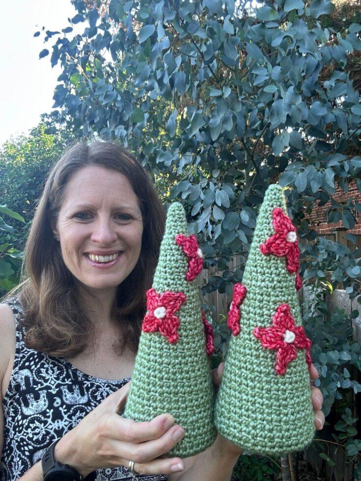 A lady holds 2 crochet Christmas tree cones with red flowers on them