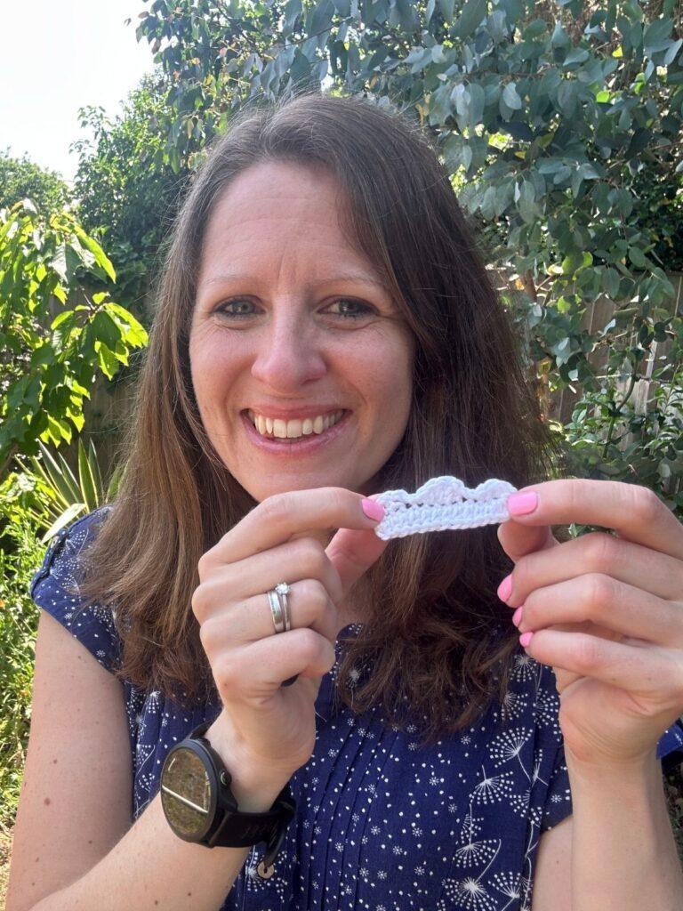 A person holds a small white crochet cloud in 2 hands