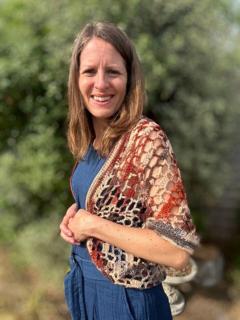 A lady stands sideways wearing a crochet earth-toned cocoon cardigan