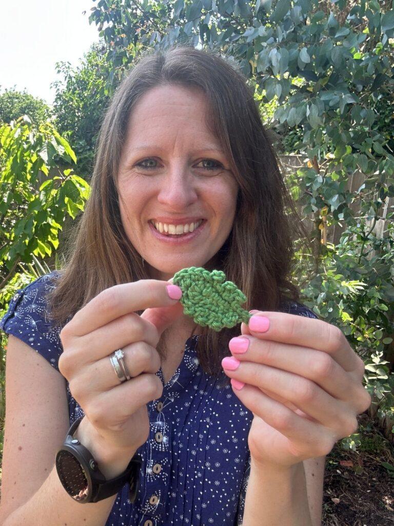 A person holds a crochet daisy leaf in her hand