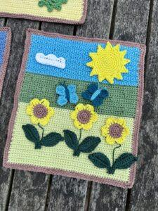 A crochet landscape showing fields, butterflies, sunflowers, and sun