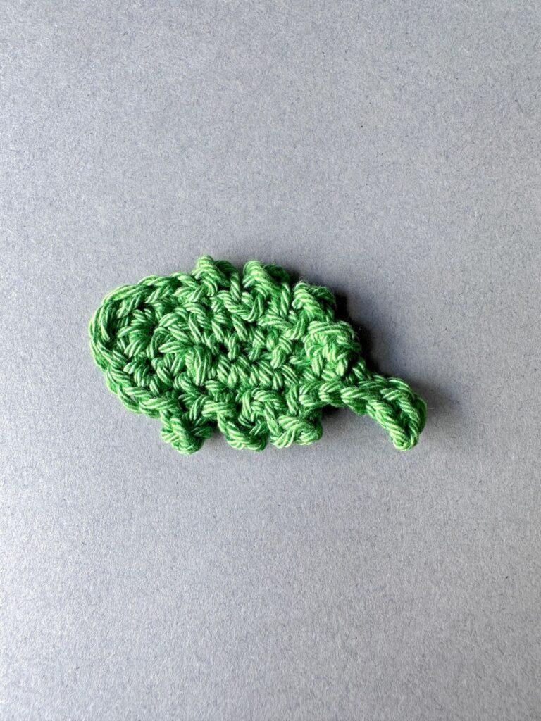 A green crochet leaf lays on a grey background