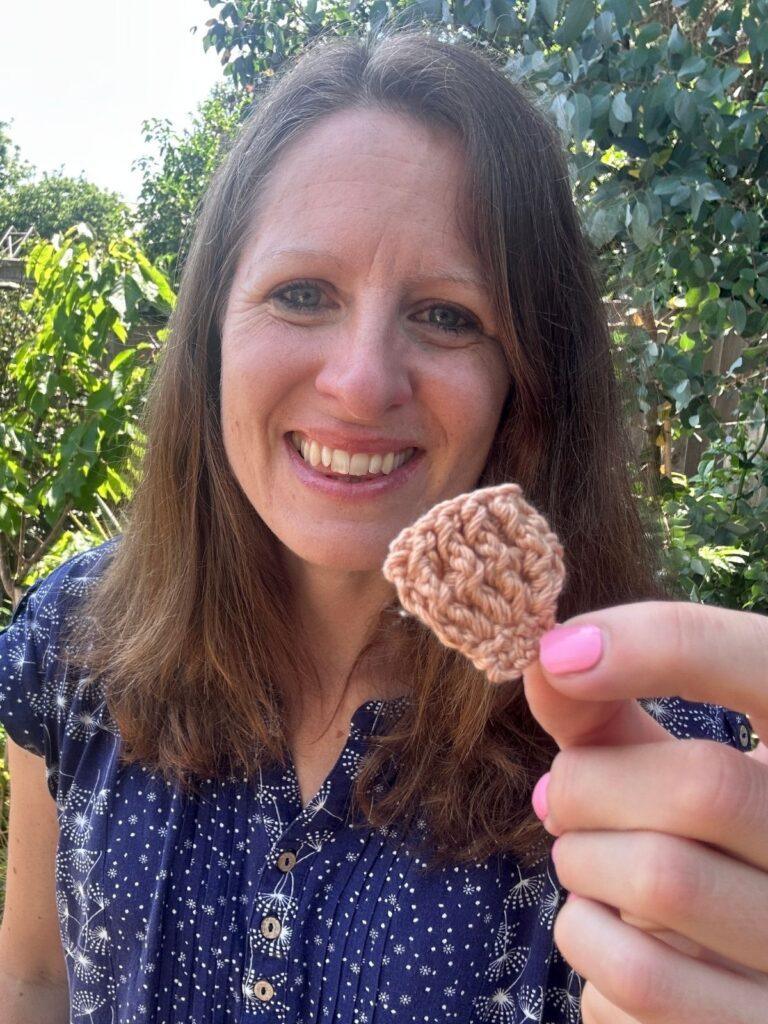 A lady holds a small crochet shell in beige yarn in her hands