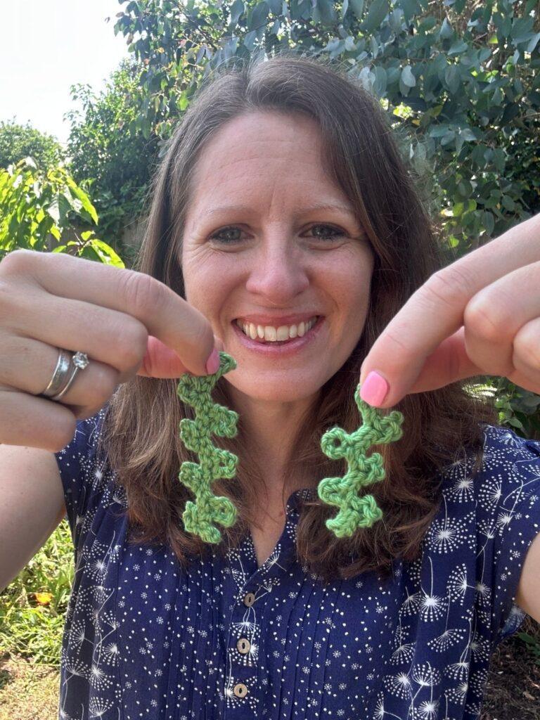 A lady holds up 2 strands of green crochet seaweed