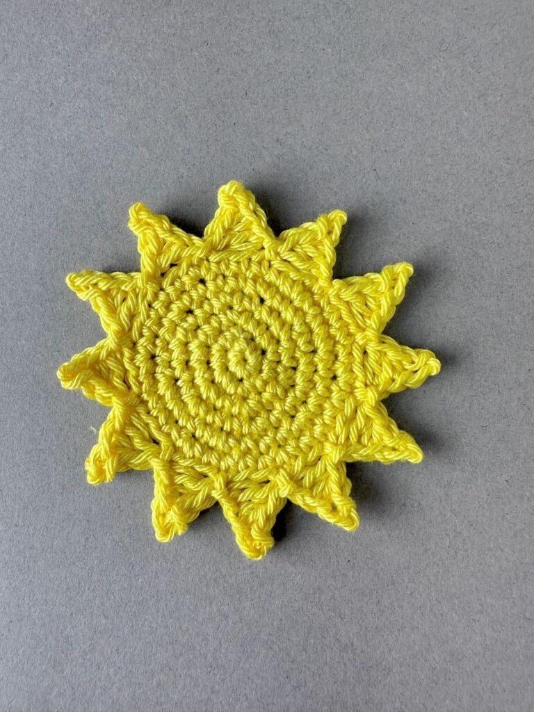 A bright yellow crochet sun on a grey background