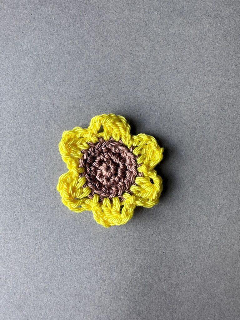 A yellow and brown crochet sunflower motif on a grey background