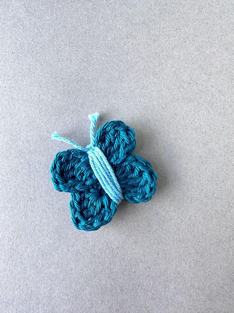A teal coloured crochet butterfly with blue centre on a grey background