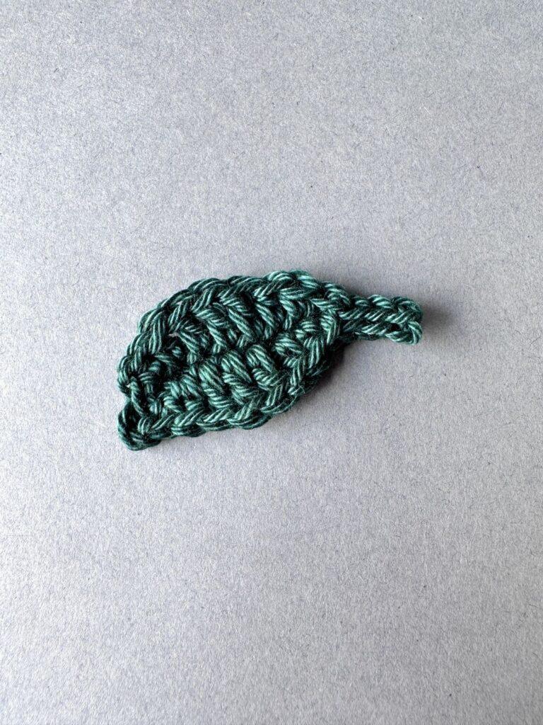 A dark green crochet leaf on a grey background