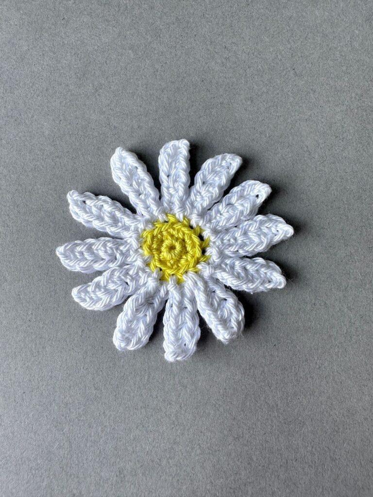A large crochet daisy (oxeye daisy) in yellow and white is on a grey background