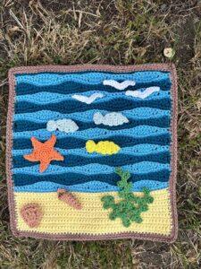A crochet scene of the seaside with applique starfish, fish, shells and seaweed
